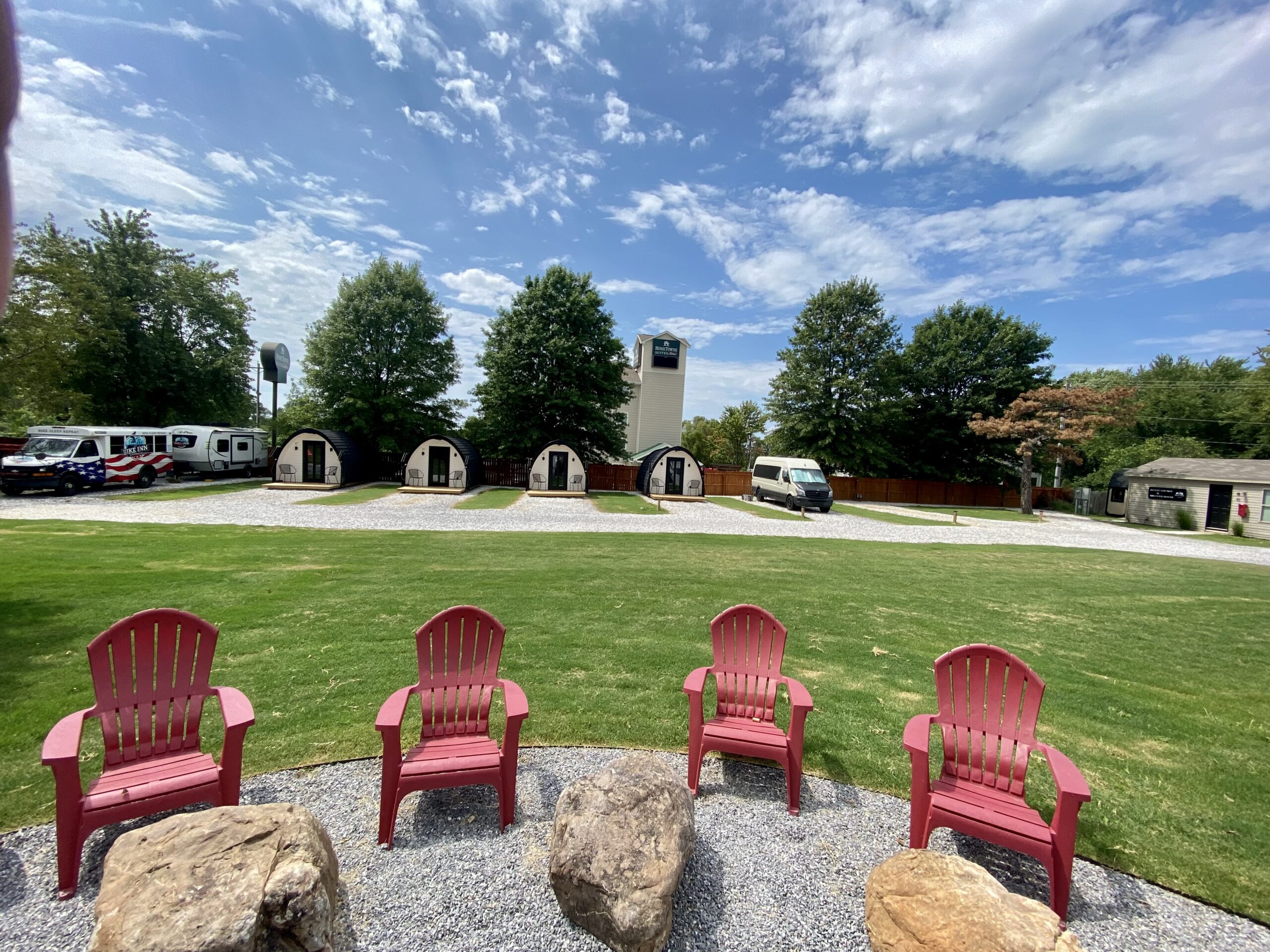 Backyard fire pit ringed by red Adirondack chairs with glamping cabins behind it at The Bike Inn in Bentonville, Arkansas